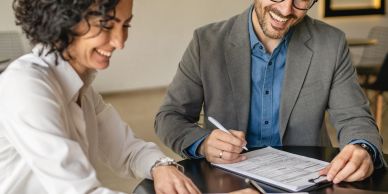 Two professionals smiling and discussing a document at a table.